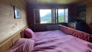 Habitación de cabaña de madera con una cama, una ventana con vista a la montaña, un escritorio y un radiador.