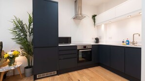 A modern kitchen with dark cabinetry, a stainless steel range hood, a built-in oven, and a sink with a faucet. - Comfty 1 Bedroom Apartment (Southampton)