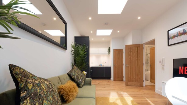 A modern living room with a sofa, a coffee table, and a TV. There is a kitchen in the background with cabinets and a sink. - Comfty 1 Bedroom Apartment (Southampton)