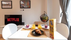 A modern room with a white table set for breakfast, a TV displaying 'NETFLIX', and framed artwork on the wall. - Comfty 1 Bedroom Apartment (Southampton)