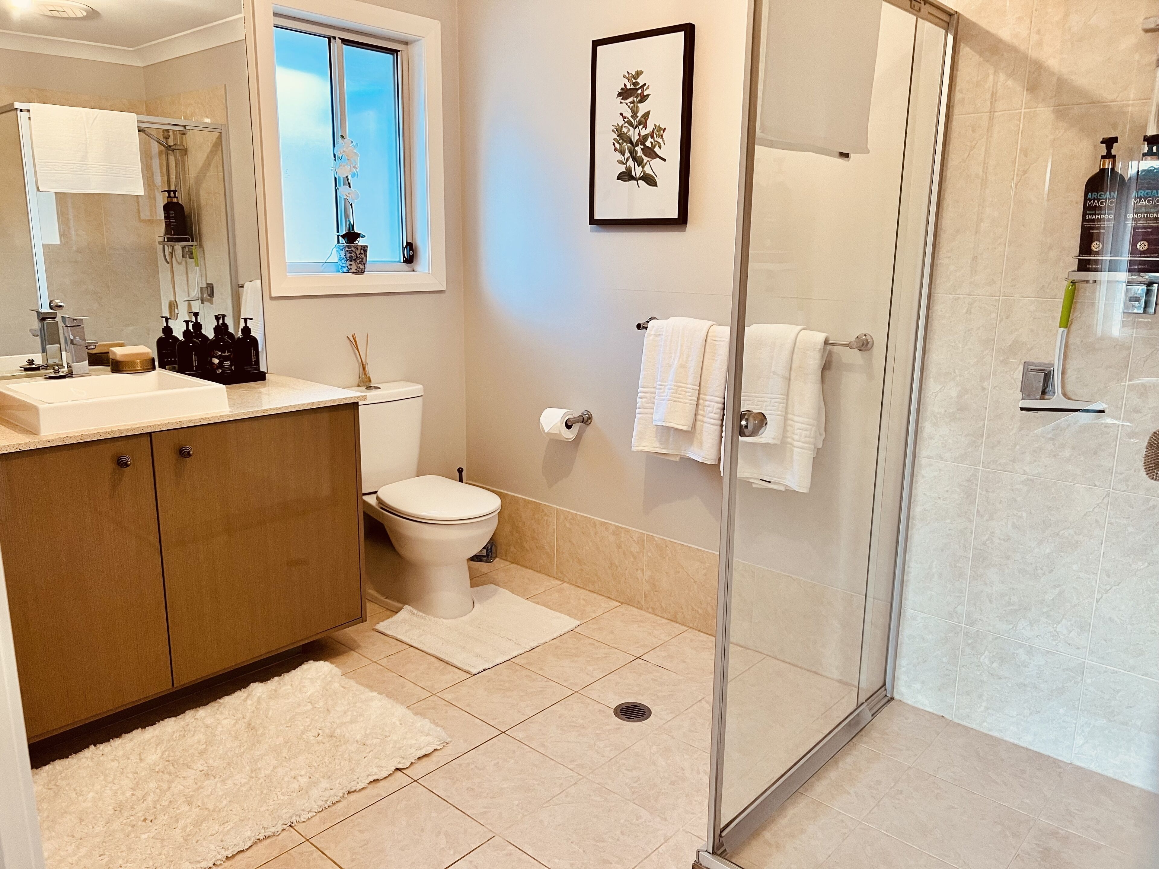 Un bagno moderno con box doccia in vetro, un water, un lavandino con mobile contenitore e una finestra con un'orchidea in vaso.