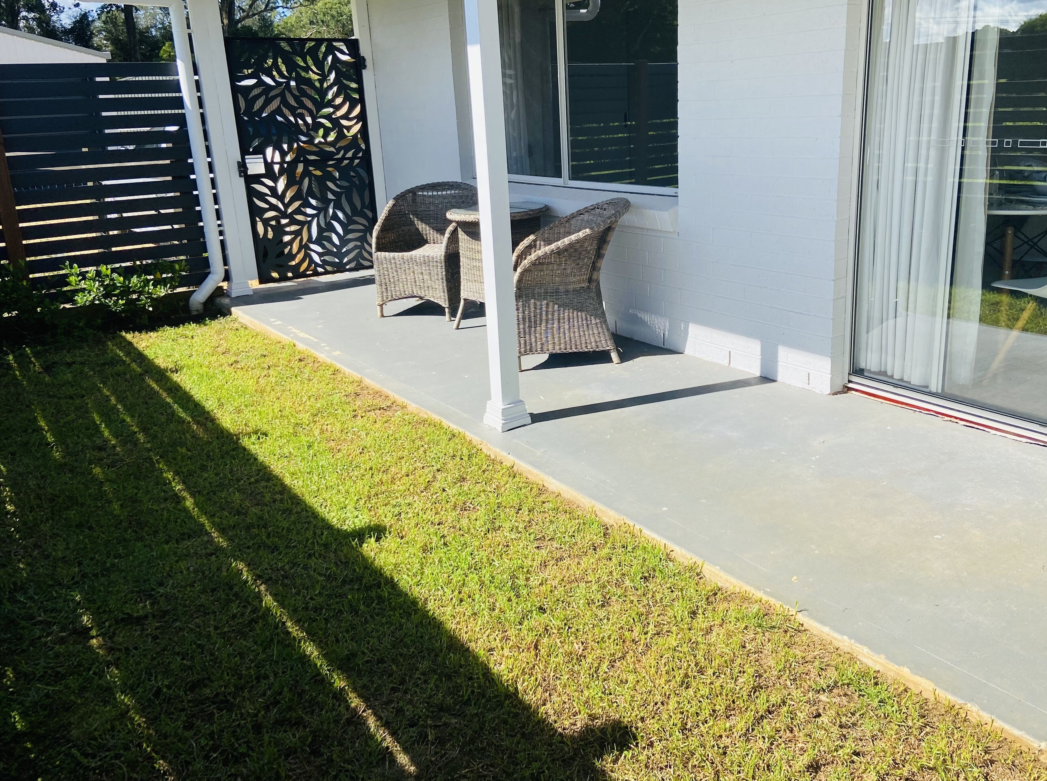 A covered patio area with wicker furniture and a glass door leading to a garden.