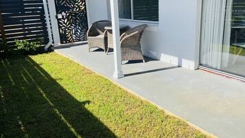 A covered patio area with wicker furniture and a glass door leading to a garden.