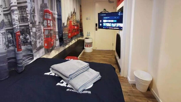 A hotel room with a bed, a flat-screen TV, a wall with a London-themed mural, and a small trash bin. - KMB hostel (Kowloon)