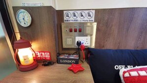 A wooden bedside table with a red lantern, a 'LONDON' box, a red star-shaped object, and a pillow with 'OFF-BLUE' text. - KMB hostel (Kowloon)
