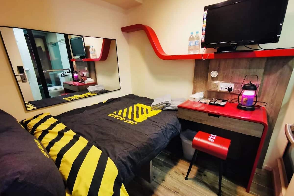 Une chambre d’hôtel de taille réduite, comprenant un lit, un bureau, un miroir, une télévision et un petit tabouret.