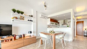 A modern living room with a TV, books, and a dining area with a table and chairs.