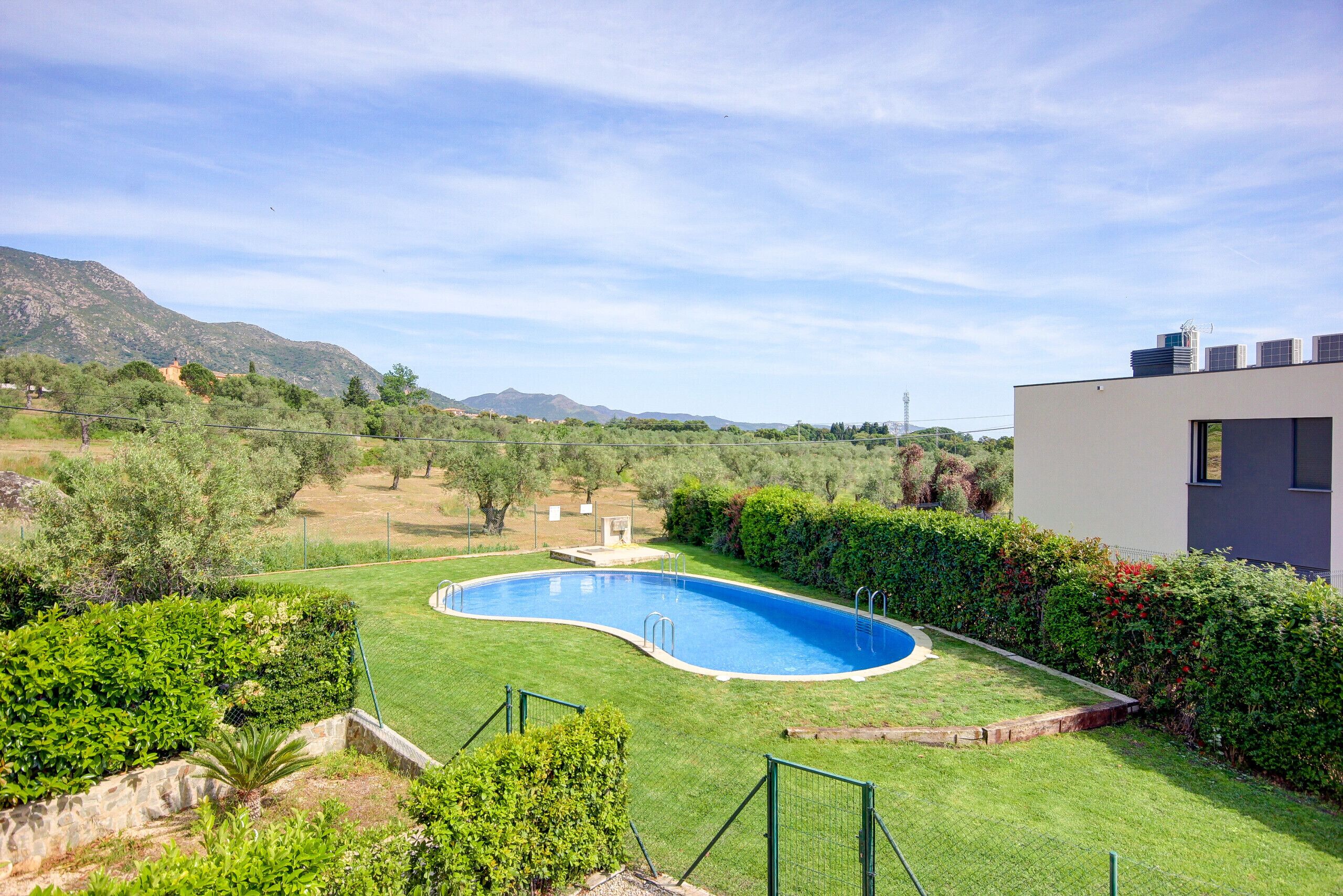 A swimming pool surrounded by well-maintained grass and hedges, with mountains in the background.