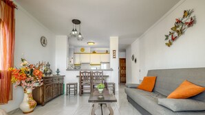 Ein Wohnzimmer mit grauem Sofa, orangefarbenen Kissen, einem Holztisch und einer Blumenkomposition.