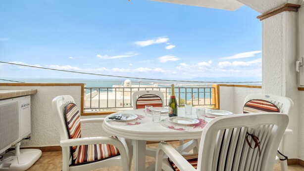 Ein Balkon mit einem Tisch für zwei Personen, Stühle mit gestreiften Kissen, einer Champagnerflasche und Blick aufs Meer.