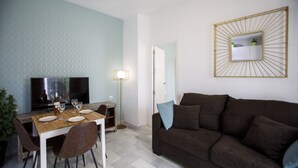 A living room with a brown sofa, a dining table set with plates and glasses, a TV, and a lamp. - Rentalsevilla Escapada en San Luis (Sevilla)