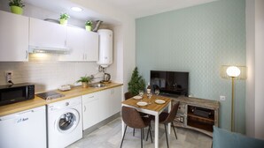 A compact kitchen with a washing machine, microwave, and a dining area with a table and chairs. - Rentalsevilla Escapada en San Luis (Sevilla)