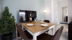 A dining area with a wooden table set for two, a television, and a potted plant. - Rentalsevilla Escapada en San Luis (Sevilla)