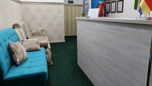 A reception area with a blue sofa, patterned cushions, a reception desk, framed certificates, and a clock. - Semurg Hotel (Tashkent)