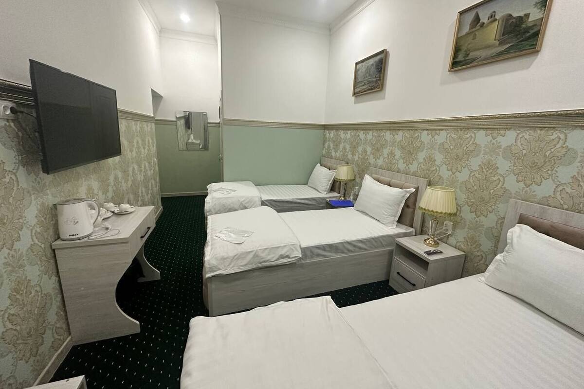 Una habitación de hotel con tres camas, un televisor de pantalla plana, un cuadro en la pared y una mesita de noche con lámpara.