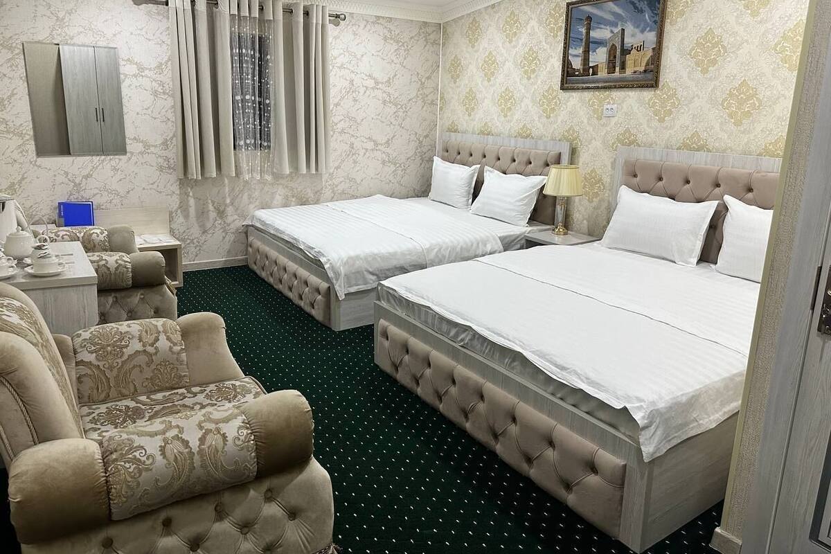 Habitación de hotel con dos camas, un sofá, un escritorio con lámpara y un cuadro en la pared.