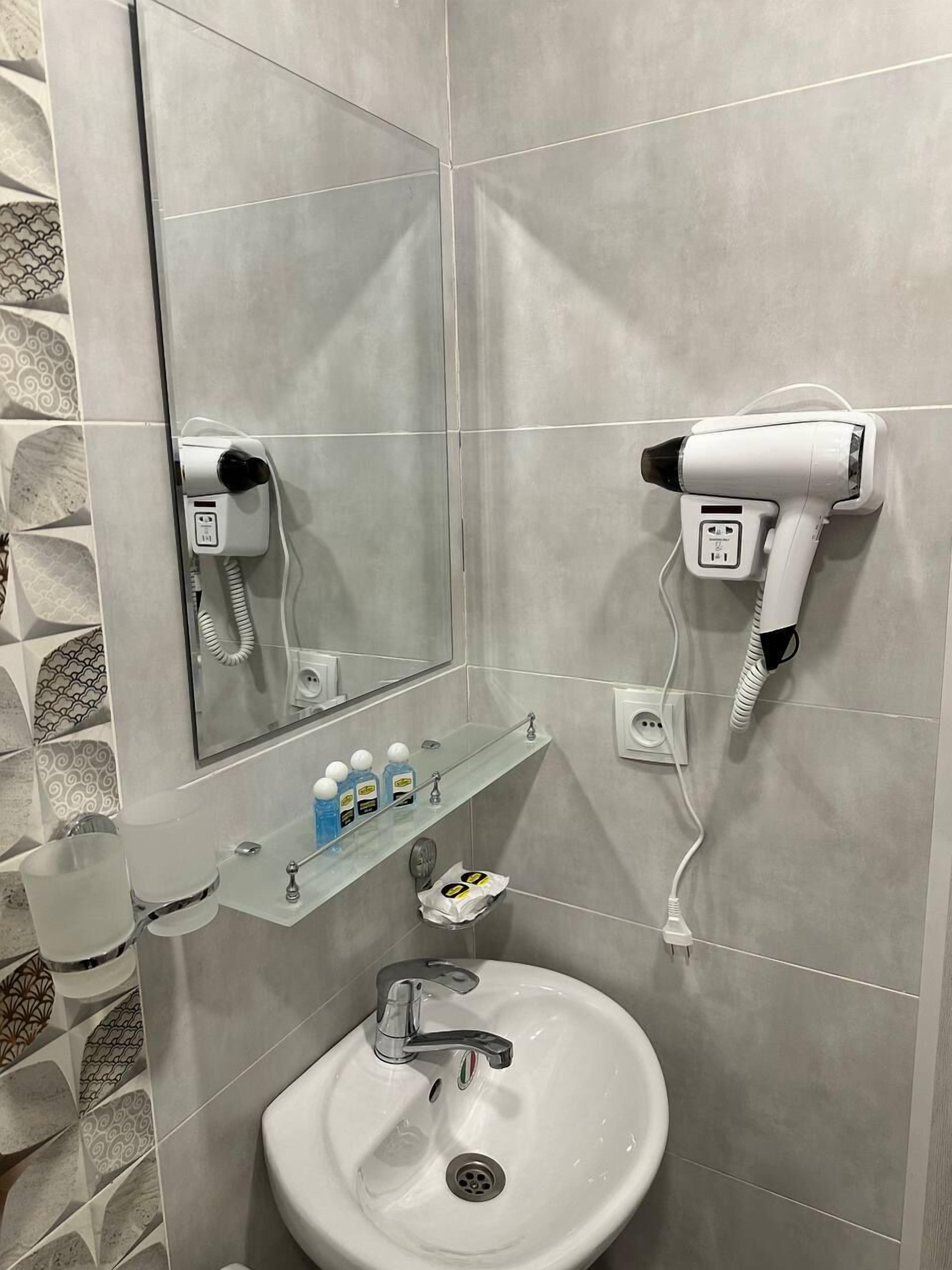A bathroom with a sink, mirror, hairdryer, and a shelf with toiletries.