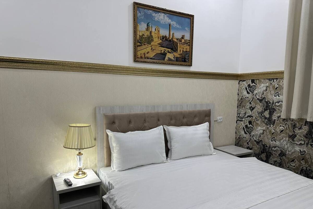 Habitación de hotel con cama, mesita de noche con lámpara, un cuadro en la pared y un papel tapiz con diseño de mármol.