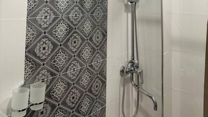 A shower with a rain shower head and handheld shower attachment, a towel rack with two towels, and a patterned tile backsplash. - Semurg Hotel (Tashkent)