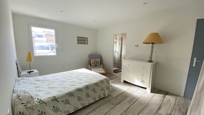 A bedroom with a bed, a dresser, a mirror, a lamp, and a window. - Seafront house (Fleury)