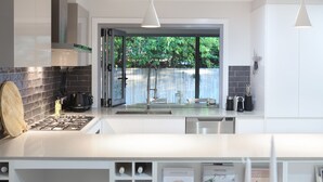 Une cuisine moderne équipée d’une cuisinière à gaz, de meubles blancs et offrant une vue sur la verdure environnante.
