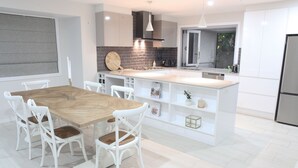 Une cuisine moderne dotée d’un îlot central, de meubles blancs et d’un coin repas avec des chaises blanches.
