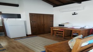 A compact kitchen with a white refrigerator, a wooden table with a microwave, and a wooden cabinet. - Oxen Car House 1 Bedroom (Capelo)