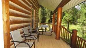 A wooden deck with metal chairs and a table, surrounded by a wooden railing, overlooking a forested area. - The Hideaway Hostel near Yellowstone (Island Park)