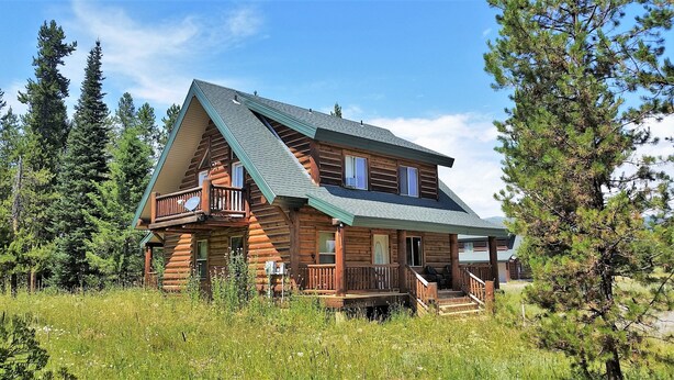 A log cabin with a balcony, surrounded by trees and a grassy field. - The Hideaway Hostel near Yellowstone (Island Park)