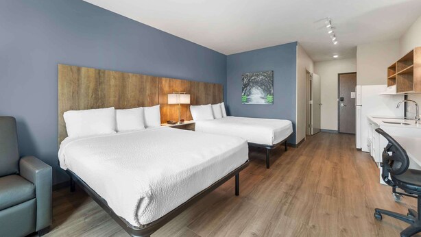 A hotel room with two beds, a desk, a chair, a lamp, and a painting on the wall.