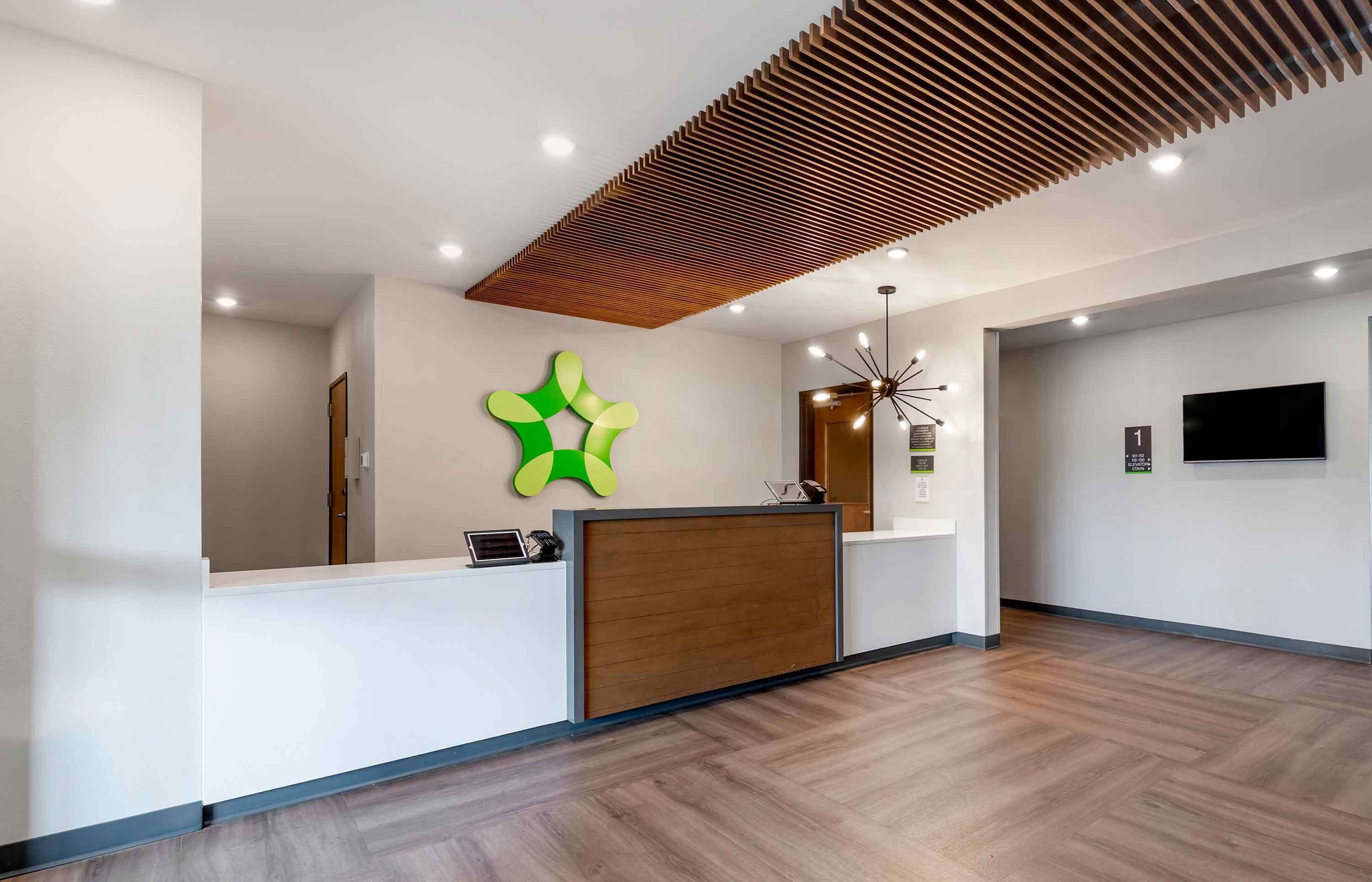 Un espace d’accueil moderne avec un comptoir en bois, une œuvre d’art abstraite verte au mur et un plafond au design à lattes.