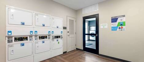 A laundry room with multiple washing machines, a door, and a poster on the wall.