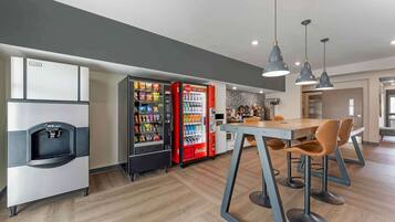Una cocina moderna con un refrigerador, un refrigerador Coca-Cola y un dispensador de agua. Hay una zona de bar con taburetes y luces colgantes.