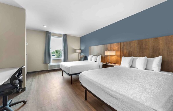A hotel room with two beds, a desk with a chair, a lamp, and a view of greenery outside. - Extended Stay America Suites - Huntsville - Madison (Madison)