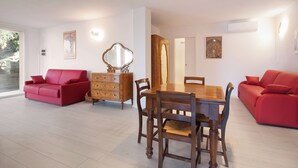 A living room with a dining table, two red sofas, a wooden dresser with a mirror, and a door leading to another room. - Villa Malù - APT Amalia - Pool and lake view (Torri del Benaco VR, Italia)