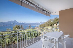 Un balcón con mesa y sillas, con vistas a un paisaje montañoso y un lago.