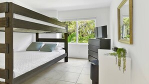 Un dormitorio con una cama individual sobre otra, un aparador, un televisor y una ventana con vista a la vegetación.