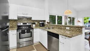 Una cocina moderna con electrodomésticos de acero inoxidable, encimeras de granito y armarios blancos.
