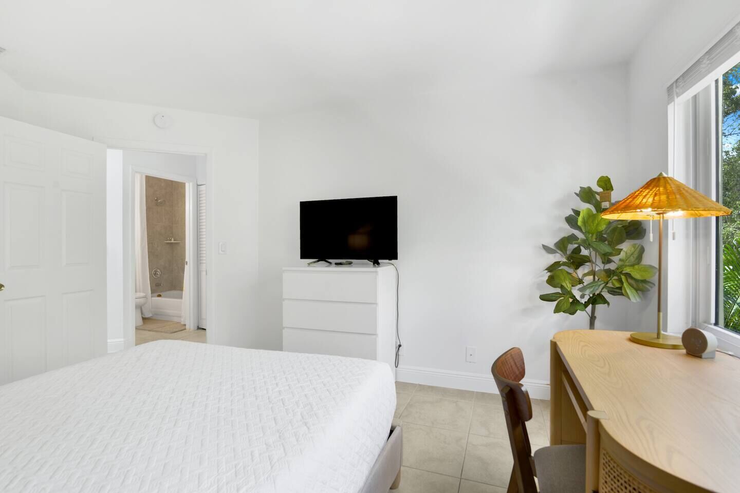 Et hotelværelse med en seng, et skrivebord med lampe, et fjernsyn og et badeværelse med bruser.