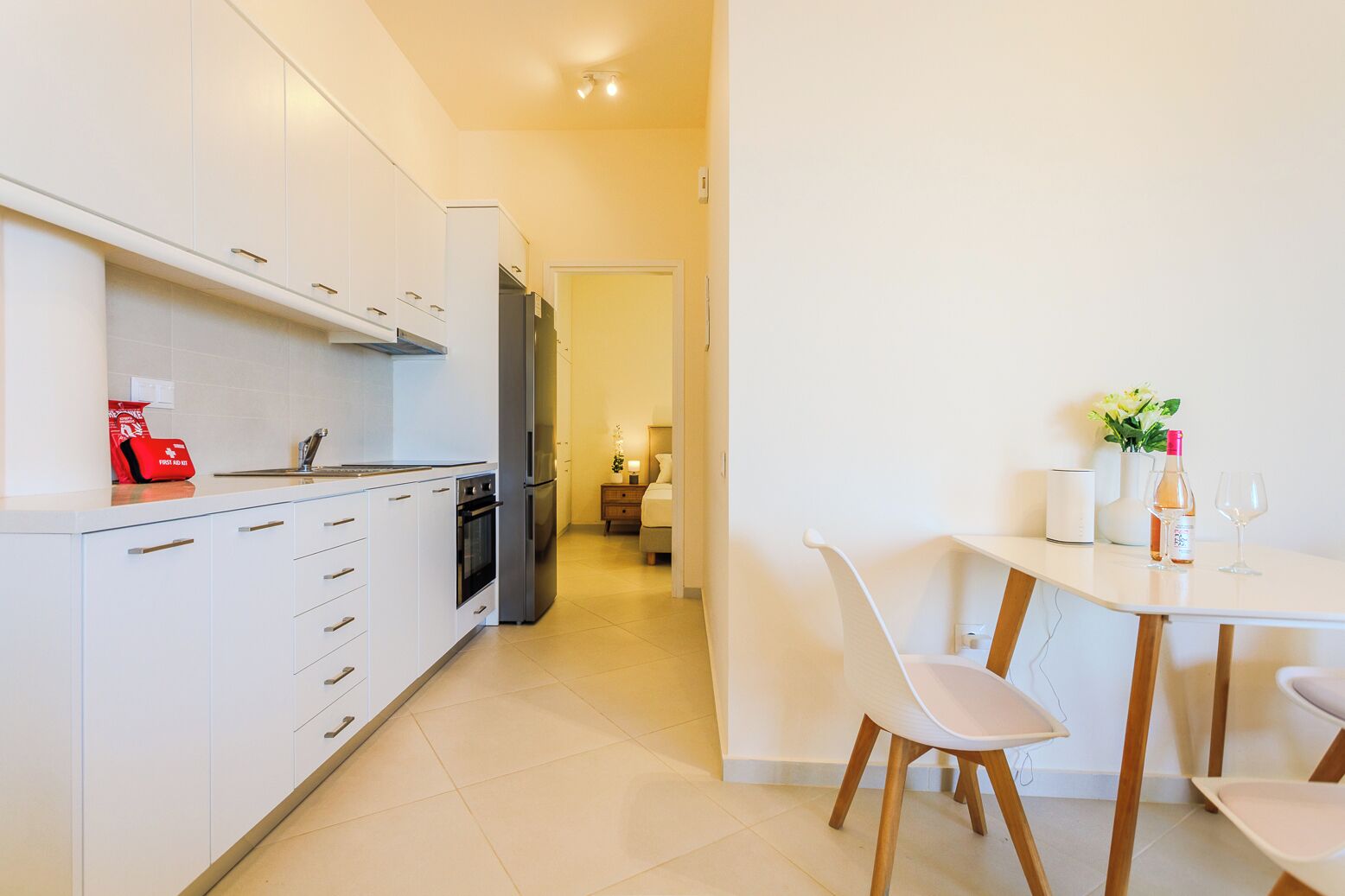 Une cuisine moderne avec des meubles blancs, un réfrigérateur et un coin repas comprenant une table et des chaises.
