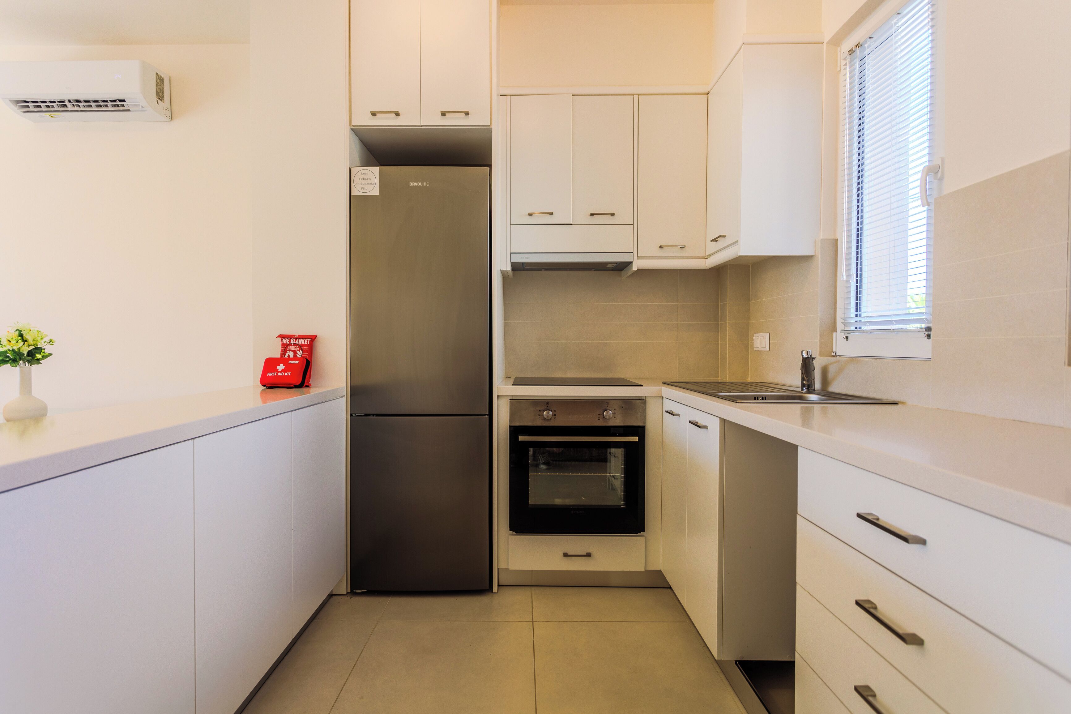 A compact kitchen with white cabinets, a stainless steel refrigerator, an oven, and a sink.