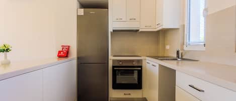 A compact kitchen with white cabinets, a stainless steel refrigerator, an oven, and a sink.