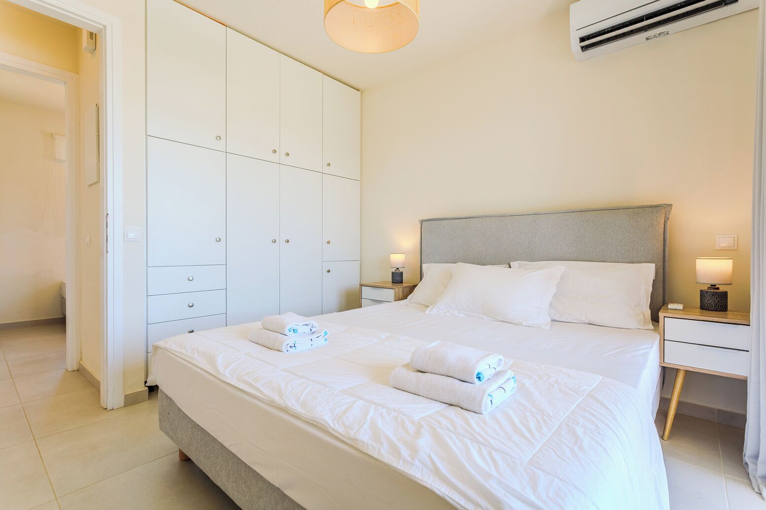 Una habitación de hotel con cama, mesitas de noche, un armario y un equipo de aire acondicionado.