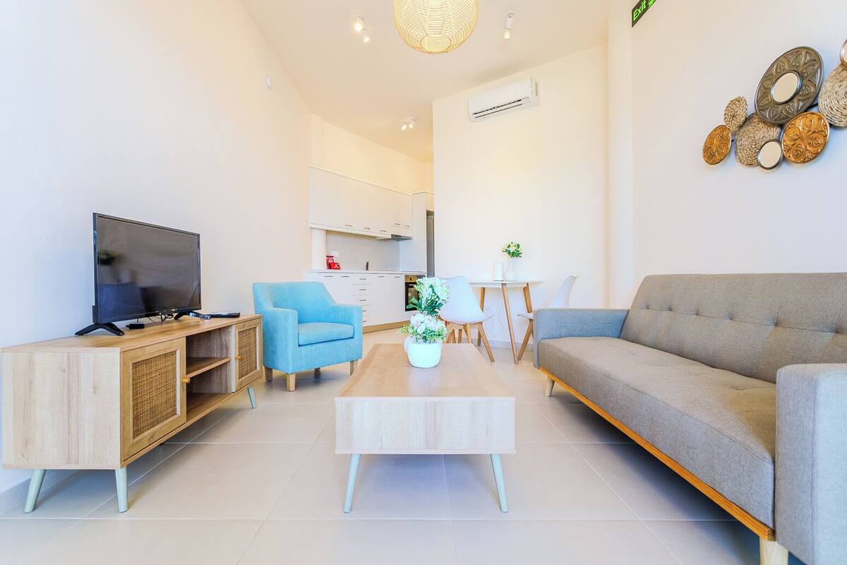 A modern living room with a TV, sofa, blue armchair, and a dining area.