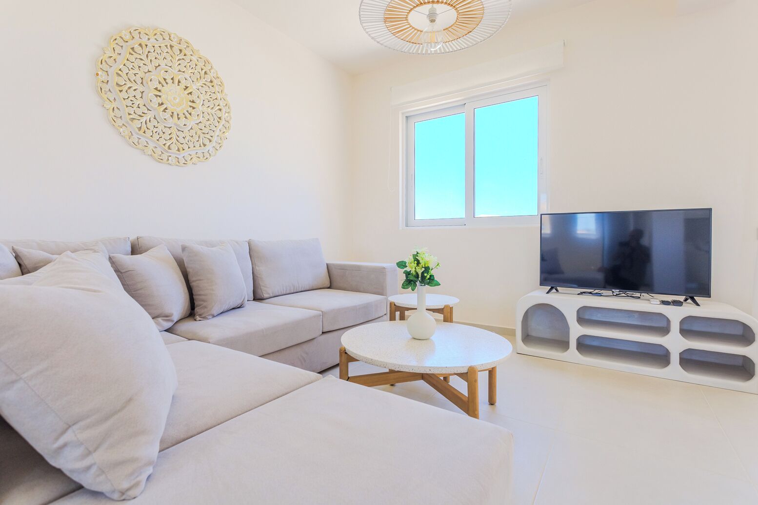 A modern living room with a sectional sofa, a round coffee table, a flat-screen TV, and a decorative wall piece.