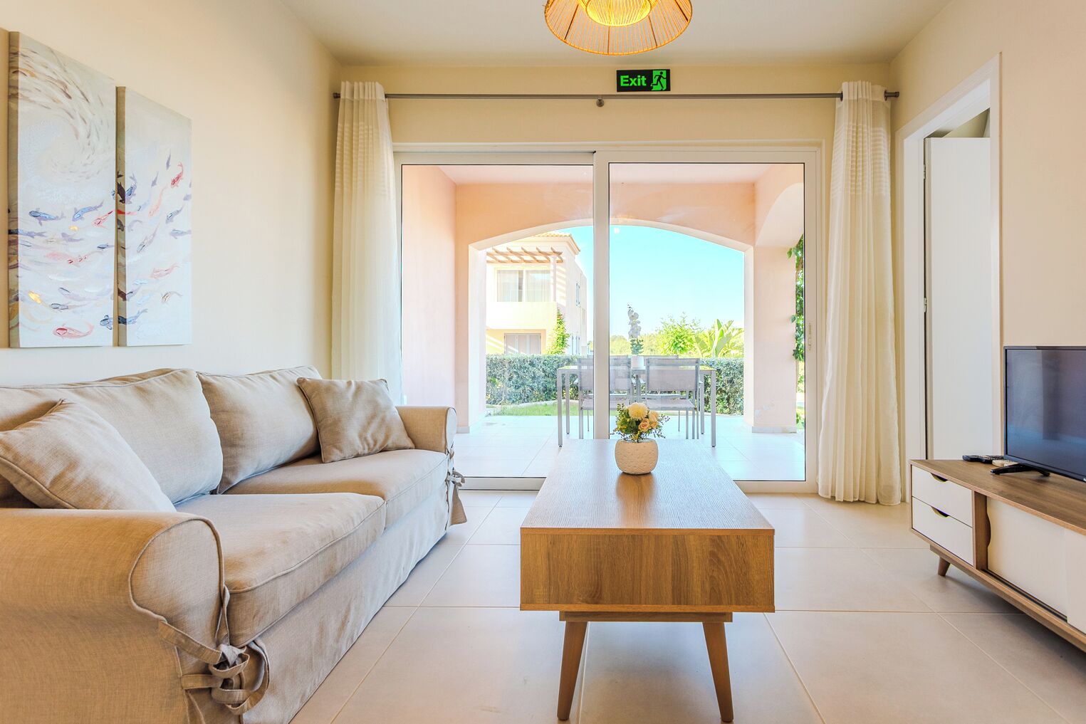 Ein Hotelzimmer mit einer Couch, einem Holztisch, einem Fernseher und Blick auf die Terrasse.