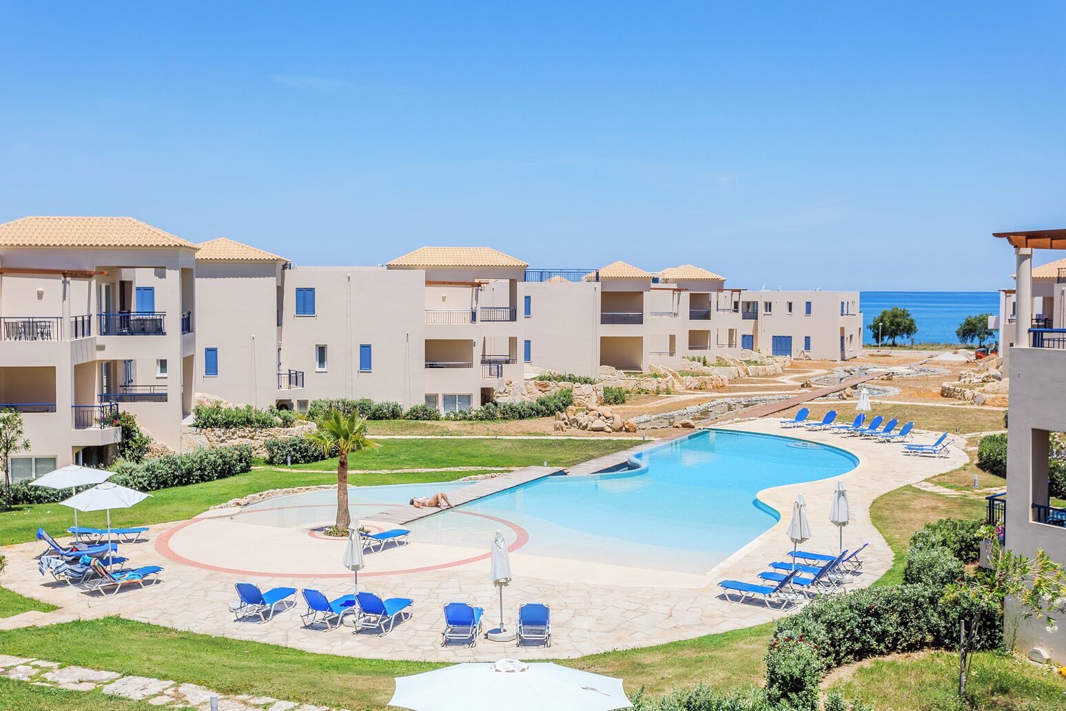 A resort with a swimming pool, lounge chairs, and a view of the sea.