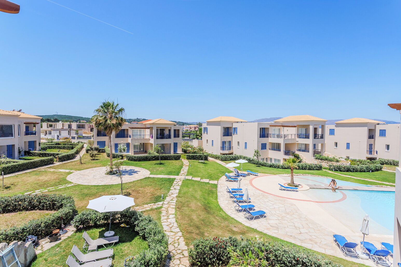 A resort with multiple two-story buildings, a swimming pool, and lounge chairs.