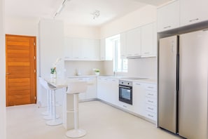 A modern kitchen with white cabinets, a stainless steel refrigerator, and a built-in oven.