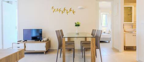 A modern living room with a flat-screen TV, a dining table with chairs, and a decorative wall piece.